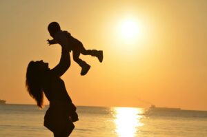 Mulher Carregando Bebê Na Praia Durante O Pôr Do Sol