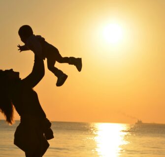 Mulher Carregando Bebê Na Praia Durante O Pôr Do Sol